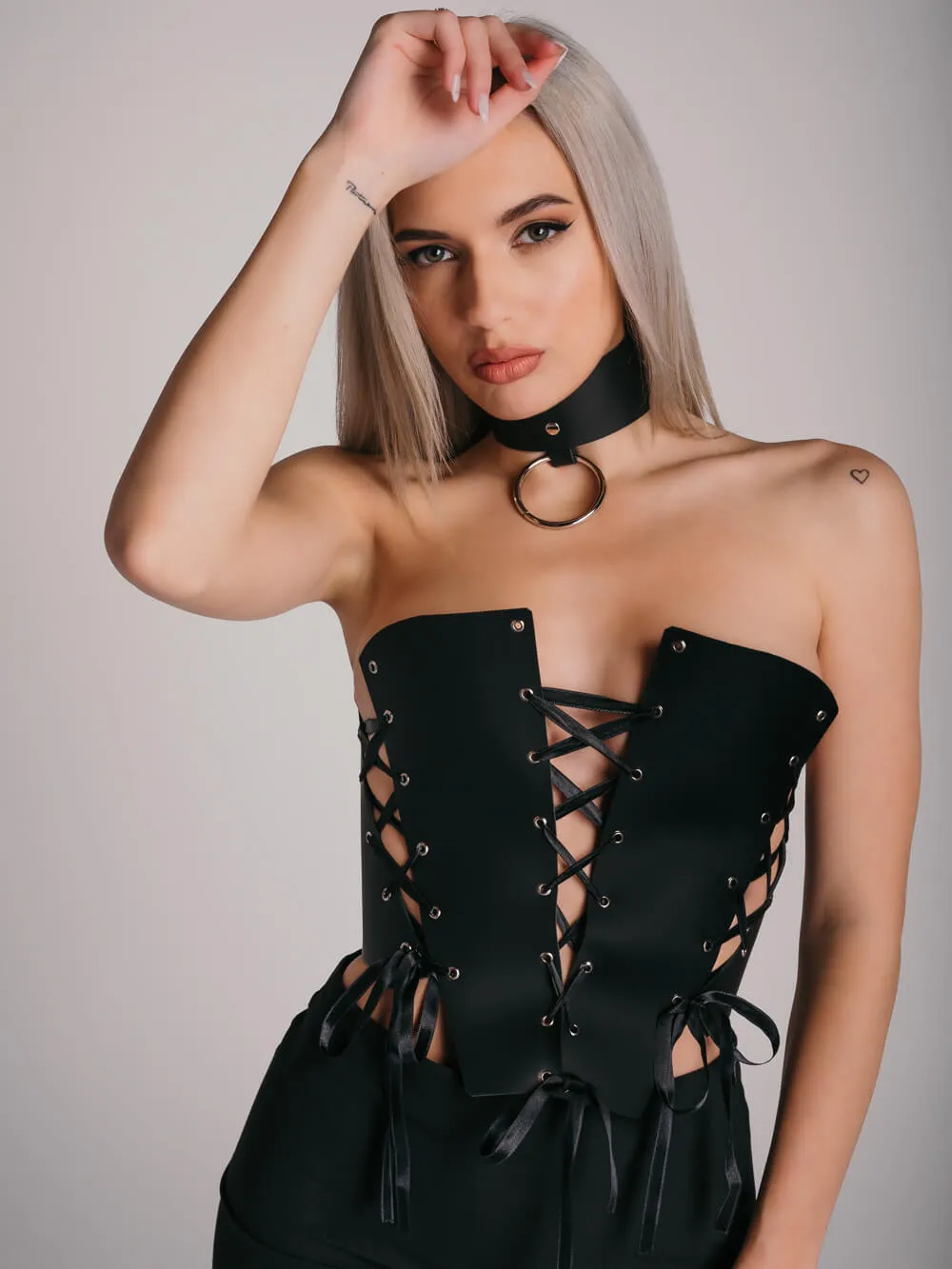 Wide black leather choker with large silver ring and massive leather corset with satin laces.
